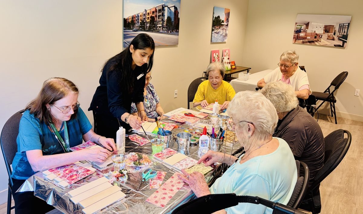Harpreet helping a group of seniors with a craft activity around a table